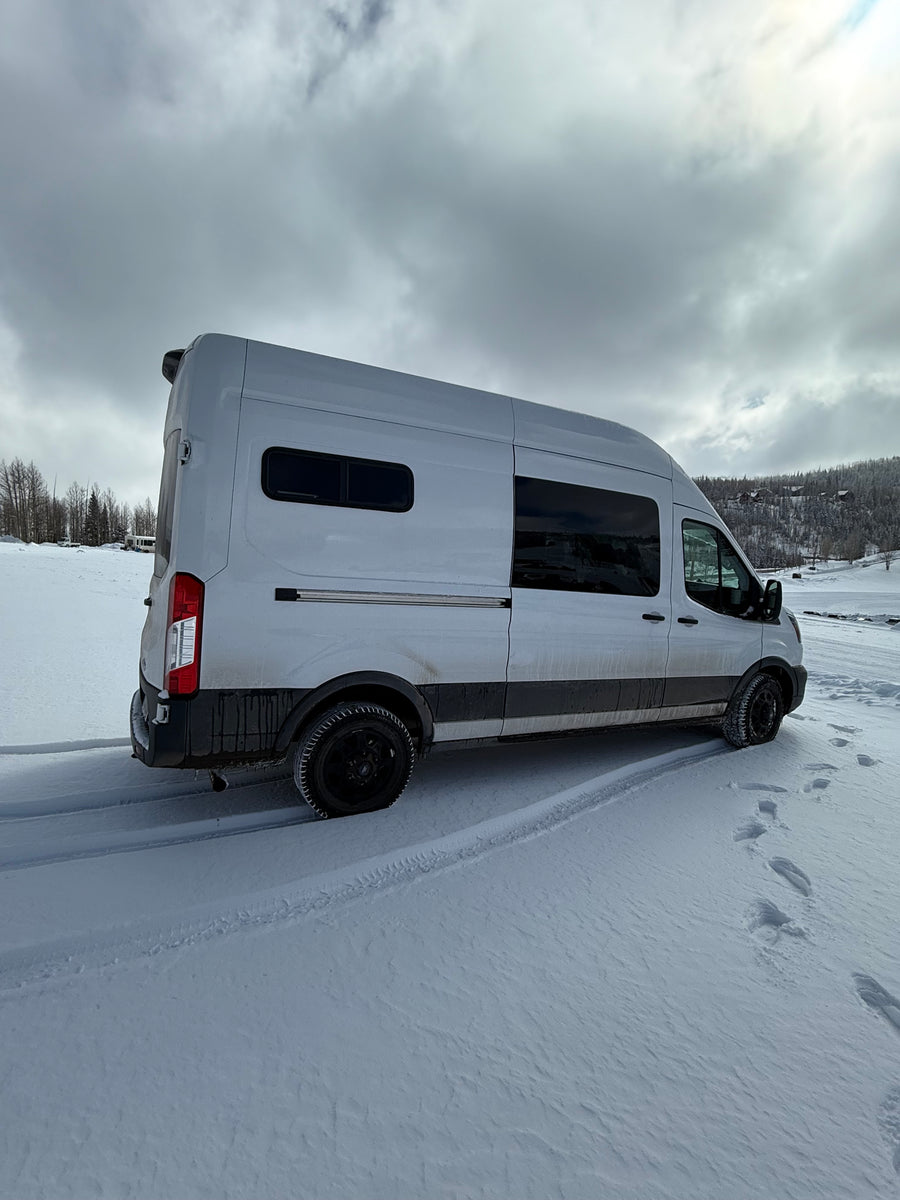 Experience winter adventures in this rugged RV rental camper van, parked in fresh snow with tire tracks and footprints.