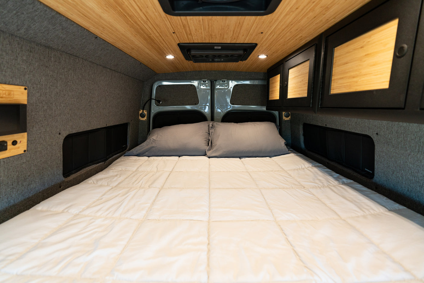 RV rental: Cozy camper van bed with wood ceiling, grey walls, integrated storage, and reading light for comfort.