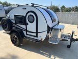 This white Boondock teardrop travel trailer, perfect for your next rv rental adventure, features off-road tires & a roof rack.