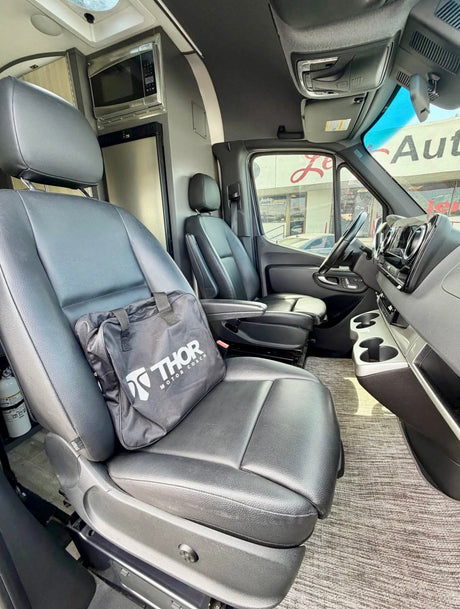 Spacious rv rental van interior featuring front captain seats, a Thor bag, built-in microwave, and fridge.