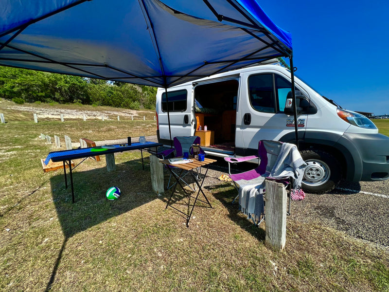 White camper van RV rental set up under a blue canopy with outdoor tables, chairs, and a volleyball, enjoying a sunny day outdoors. — photo 19