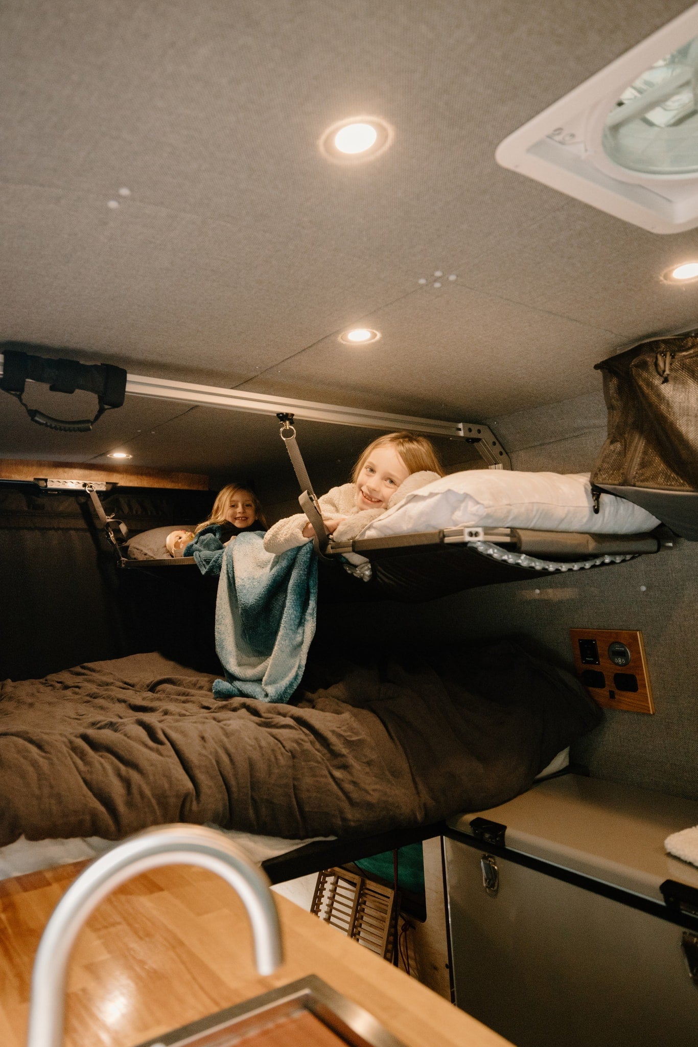 Cozy RV rental interior shows two smiling girls in bunk beds, enjoying family van life adventures. — photo 3
