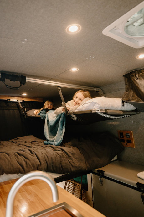 Cozy RV rental interior shows two smiling girls in bunk beds, enjoying family van life adventures.