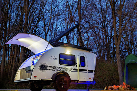 Enjoy the outdoors! This Luna Rover teardrop RV rental, fully lit, awaits adventure with a cozy campfire and tent at dusk.
