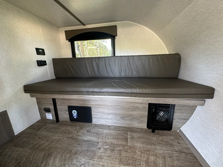 RV rental interior: long upholstered bench seat, window, wood-look floor, and floor vent, a functional living space.