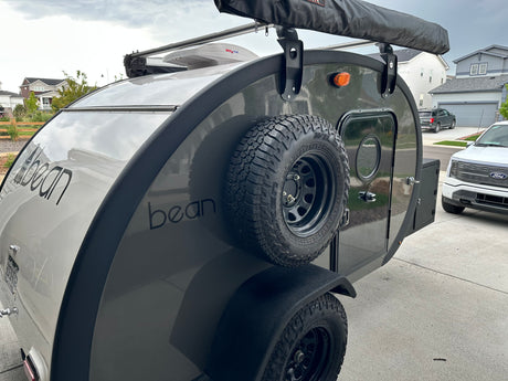 This Bean teardrop camper, a compact RV rental, features an awning and spare tire for your next adventure.