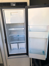 An open, empty Norcold RV refrigerator in an rv rental, showcasing its interior with shelves, door bins, and top controls.