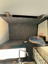 Inside an RV rental: storage cabinet with hinges above a kitchen sink, showing compact organization for essential items.