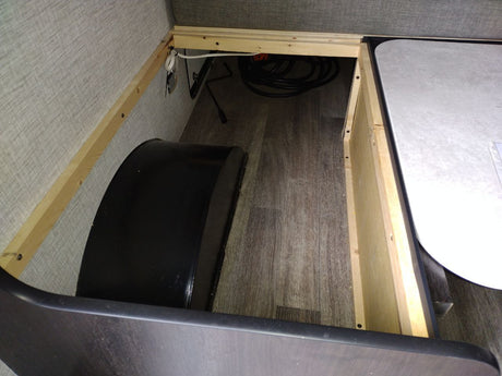 RV rental interior: A spacious under-bed storage compartment with wood framing, vinyl flooring, and a visible wheel well.