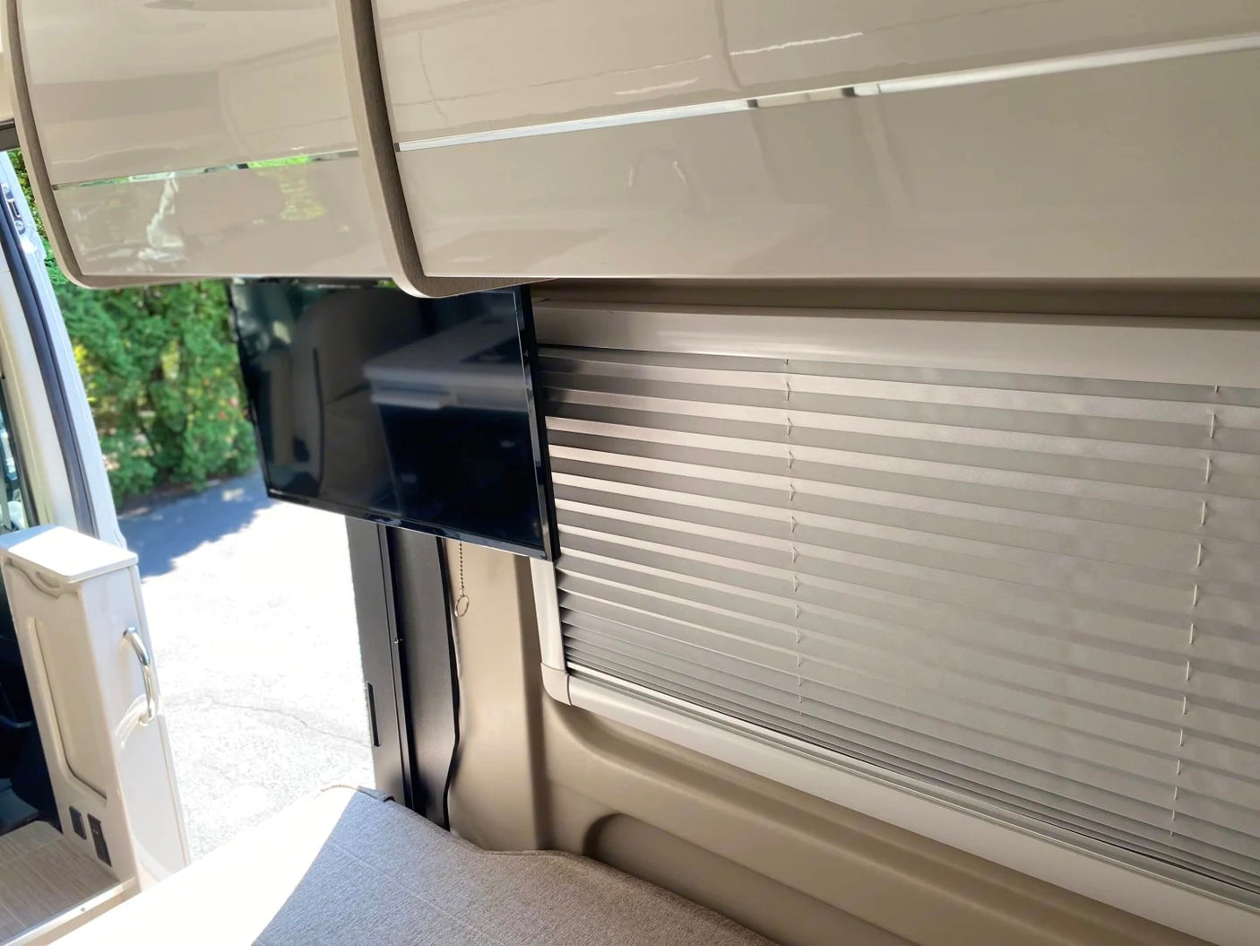 View inside an RV rental showing a mounted TV, pleated window blinds, and overhead cabinets for a comfortable journey.