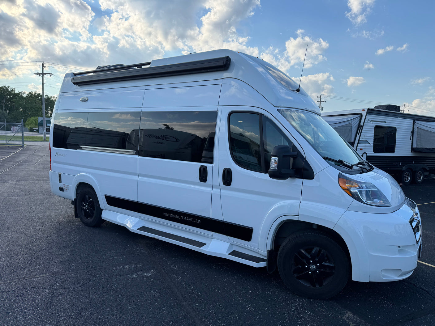 White "National Traveler" camper van, perfect for your next rv rental adventure, parked outside under a partly cloudy sky.