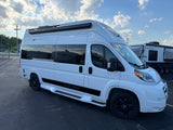 White "National Traveler" camper van, perfect for your next rv rental adventure, parked outside under a partly cloudy sky.