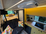 Spacious RV rental interior featuring a cozy bed, a well-equipped kitchen with sink & fridge, and a comfortable living area.