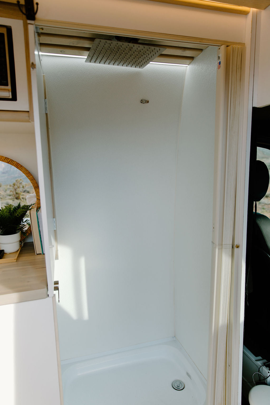 Inside an RV rental: a modern, compact shower stall. It features a rain shower head, bright LED lighting, and a white, clean interior.