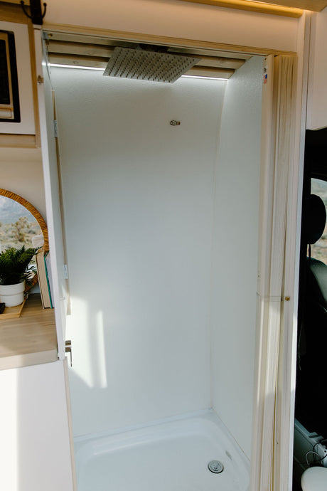 Inside an RV rental: a modern, compact shower stall. It features a rain shower head, bright LED lighting, and a white, clean interior.