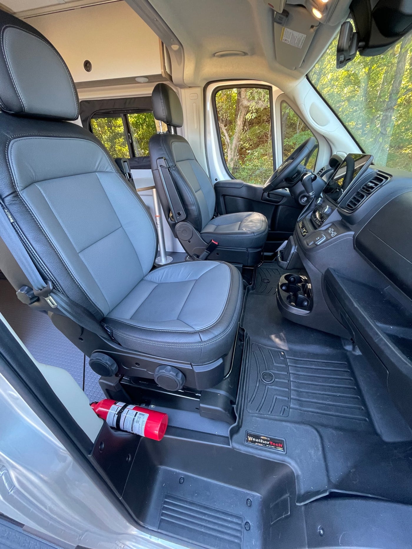 Comfortable RV rental cabin with swiveling front seats, a detailed dashboard, WeatherTech mats, and a visible fire extinguisher. — photo 16