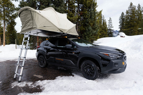 Black Subaru Crosstrek with rooftop tent parked in snow. This setup offers versatile outdoor camping, a great alternative to an rv rental.