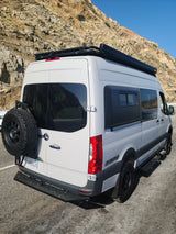 Adventure-ready Mercedes Sprinter rv rental van with off-road tires parked by rocky mountains, perfect for exploring California's coast.