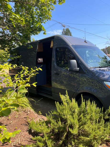 Dark grey camper van RV rental parked outdoors with side door open, showing interior.