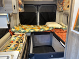 Cozy RV rental interior with a main bed, a small bunk, and a baby pack-n-play, perfect for family adventures.