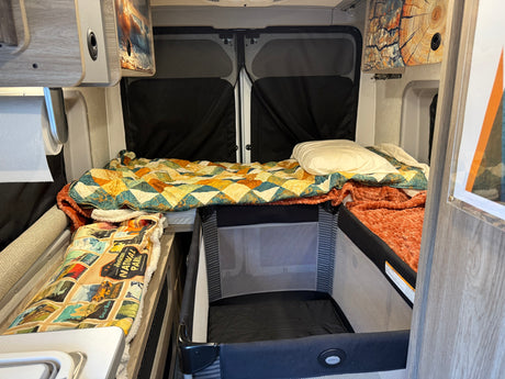 Cozy RV rental interior with a main bed, a small bunk, and a baby pack-n-play, perfect for family adventures.