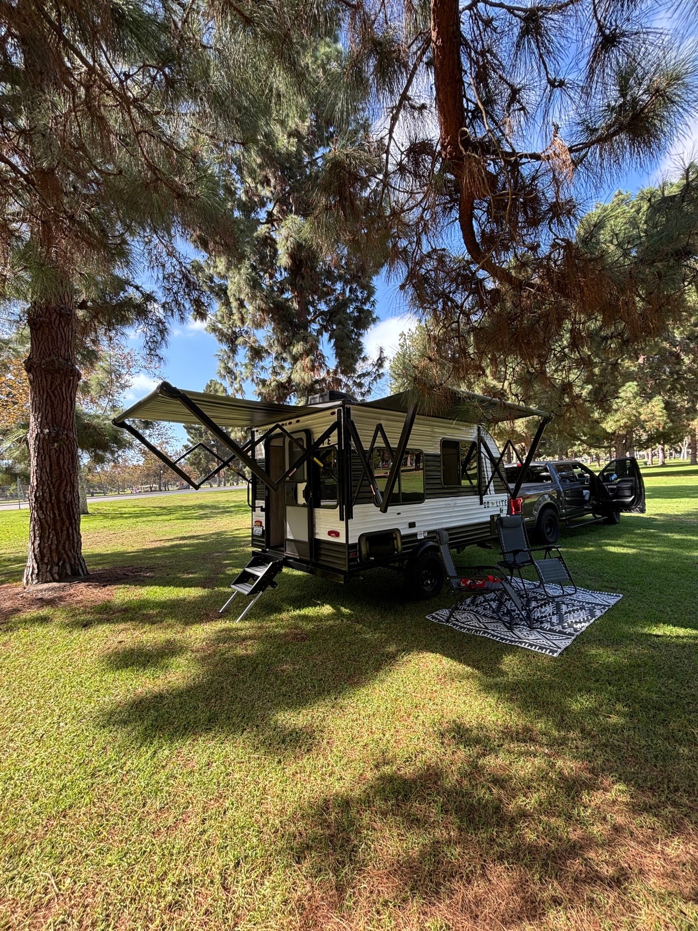 Scenic rv rental camping spot: a travel trailer, truck, and outdoor lounge setup under pine trees on green grass. — photo 2