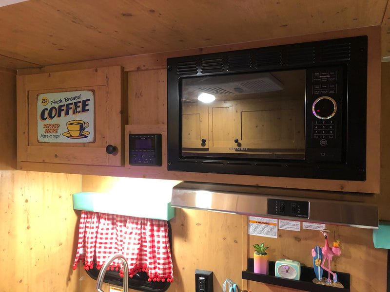 Cozy RV rental kitchenette with a microwave, coffee sign, and charming decor, perfect for meals on the go. — photo 15
