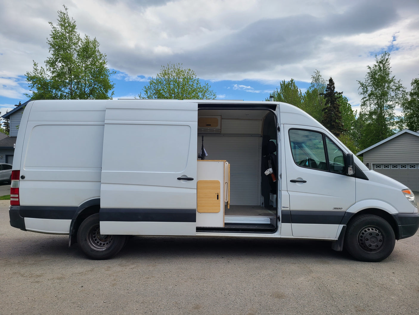White Mercedes-Benz Sprinter camper van with open side door revealing a cozy, custom interior. Ideal for RV rental adventures.