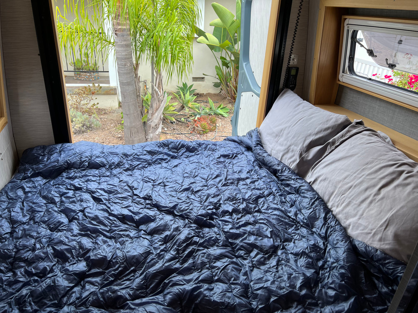 Cozy RV rental bed with a view of lush greenery outside. Ideal for a comfortable night's sleep during your adventure. — photo 12