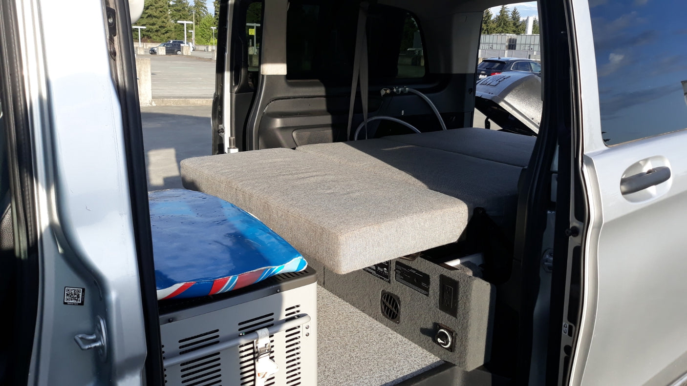 Explore this RV rental's compact camper van interior, featuring a cozy bed, portable fridge, and power station.