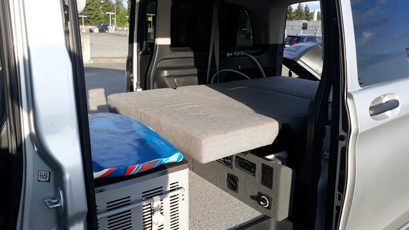 Explore this RV rental's compact camper van interior, featuring a cozy bed, portable fridge, and power station.