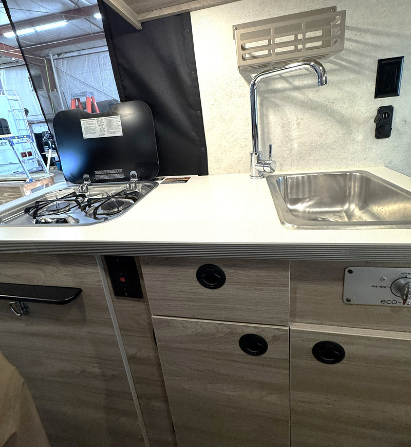 Compact RV rental kitchen features a two-burner gas stove, stainless steel sink, and light wood-grain cabinets for road trips. — photo 14