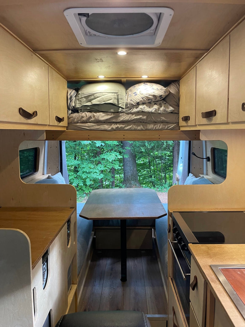 Cozy rv rental interior with a rear bed, full kitchen, dining table, and large windows offering a forest view. — photo 8