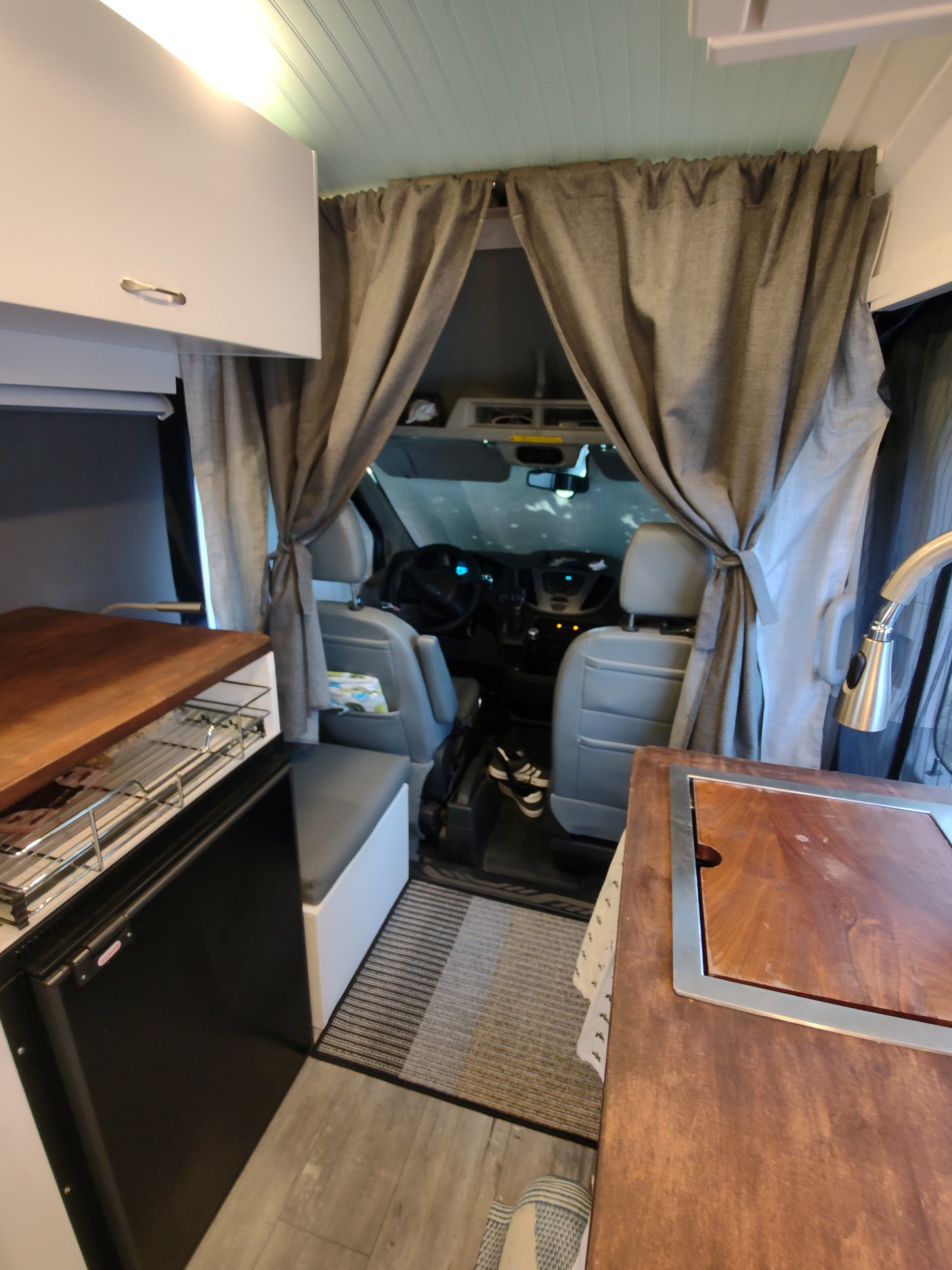 Inside a compact RV rental: a modern kitchenette on the left, grey privacy curtains, and a peek into the driver's cabin.