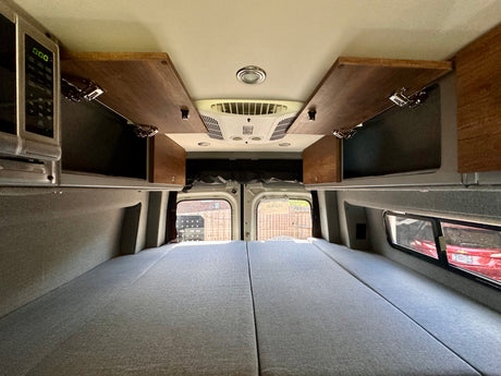 Inside an RV rental: a comfortable bed, overhead cabinets, microwave, and AC. Perfect for road trips.