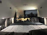 This RV rental's cozy interior features a large bed, mounted TV, and small workspace, perfect for mobile adventures.