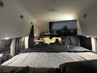 This RV rental's cozy interior features a large bed, mounted TV, and small workspace, perfect for mobile adventures.