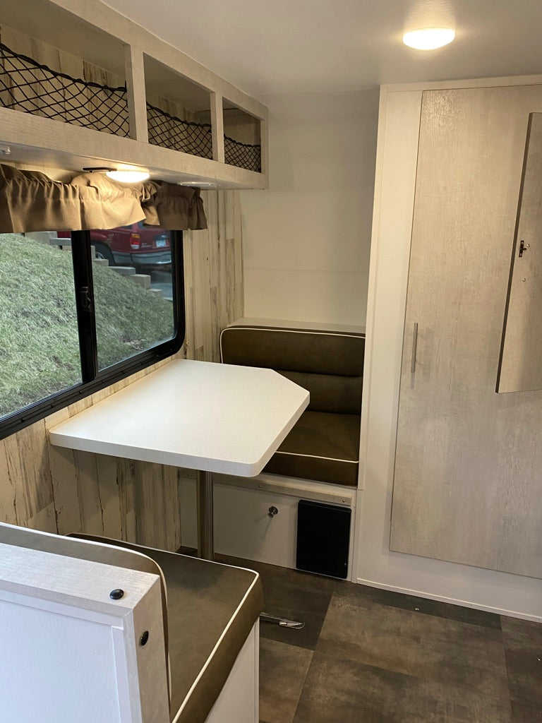 RV rental dinette: bright interior with white table, dark benches, and convenient overhead storage.