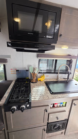 An RV rental kitchen, equipped with a Greystone microwave, range hood, gas stove, covered sink, and counter space.