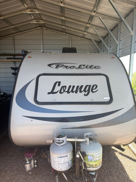 Front of a ProLite 'Lounge' travel trailer with propane tanks and hitch, safely stored under a carport. Perfect for rv rental.