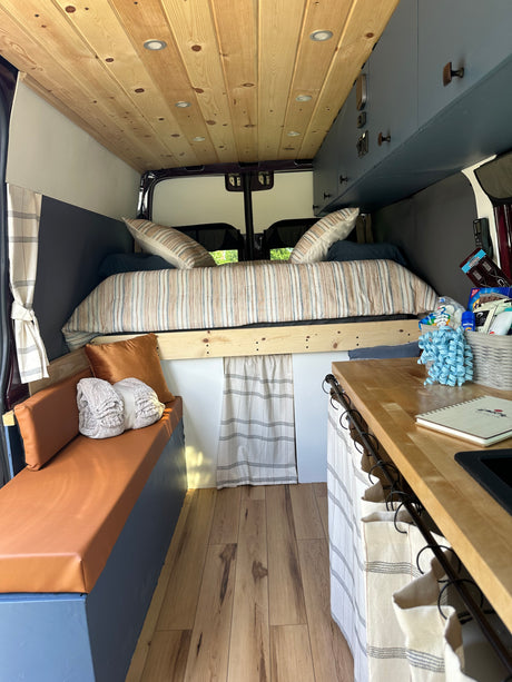 Cozy RV rental interior: wood-paneled ceiling, comfortable bed, compact kitchen, and seating area.