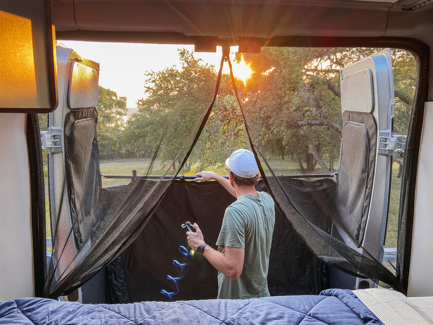 Relax in your RV rental: a man enjoys sunset views through a screen, holding a hose, ready for outdoor adventure.