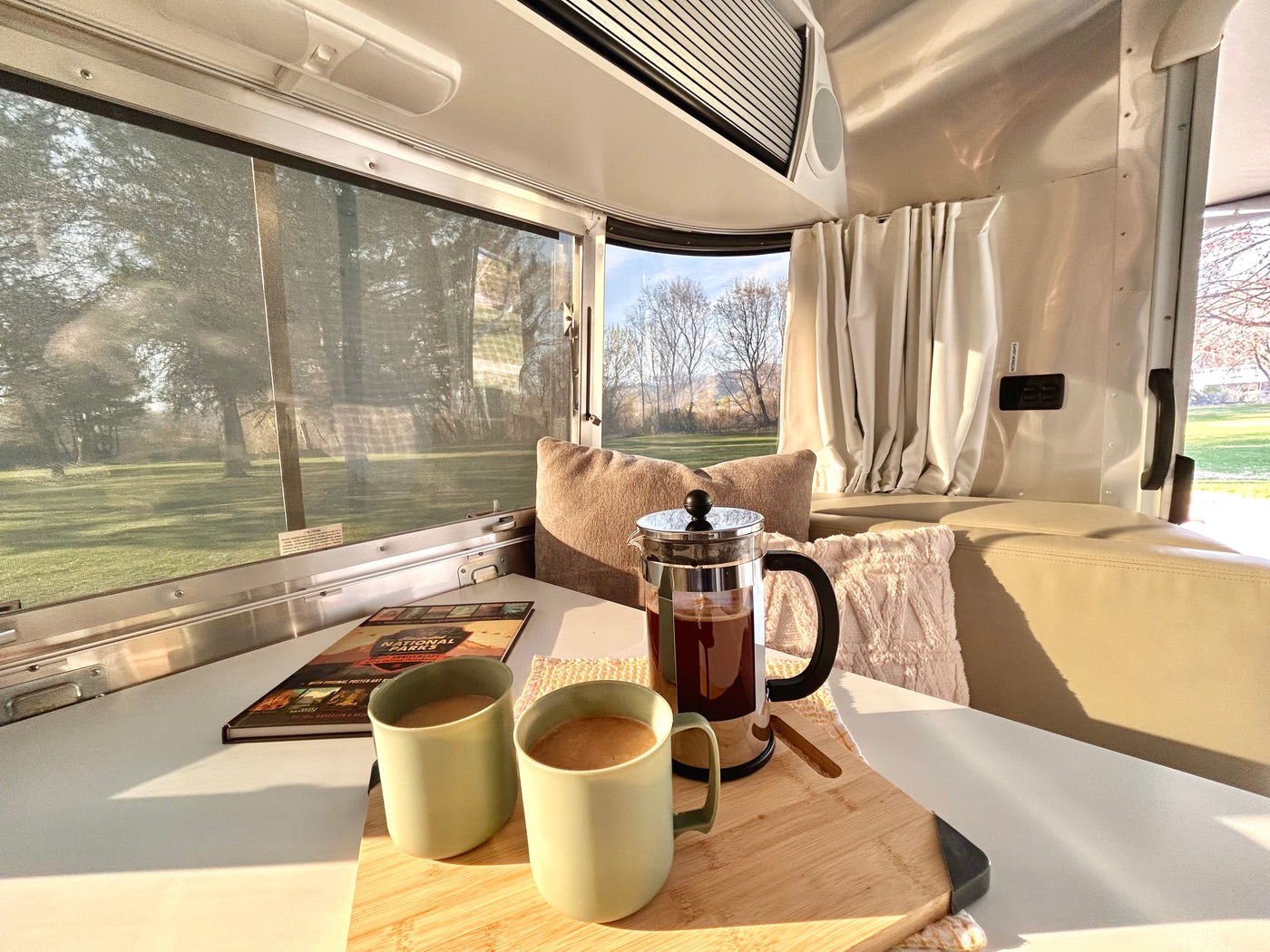 Start your travel day with coffee in this cozy RV rental. French press & mugs on table, scenic nature outside. — photo 2