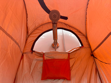Inside an RV rental's portable shower tent, featuring a showerhead and an orange storage pocket for camp essentials.