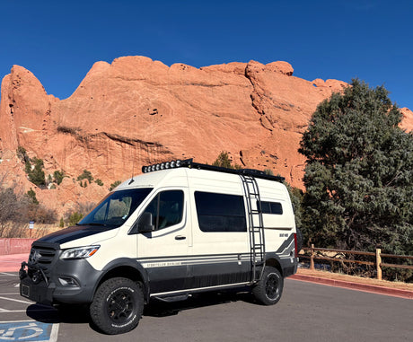 Rugged Storyteller Overland Sprinter rv rental van, equipped for adventure, parked before majestic red rock formations.