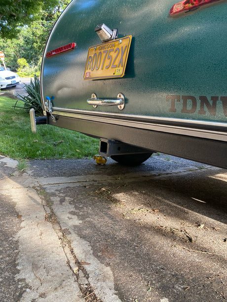 Rear view of a green rv rental camper with an Oregon license plate R00752X, hitch, and a yellow duck under it.