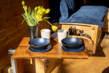 Sunlit RV rental interior: wooden walls, blue bedding, and a cozy table set with blue dishes, white mugs, and yellow tulips.