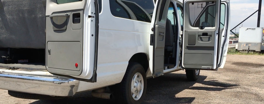 This white RV rental van has its rear and side doors open, revealing its cargo area and interior.