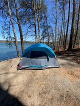 A blue tent pitched lakeside among bare trees under a clear sky. Enjoy nature camping, or an RV rental offers another way to explore.