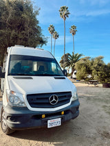 White Mercedes Sprinter RV rental at a scenic California campsite. Enjoy the palm trees & outdoor adventure!